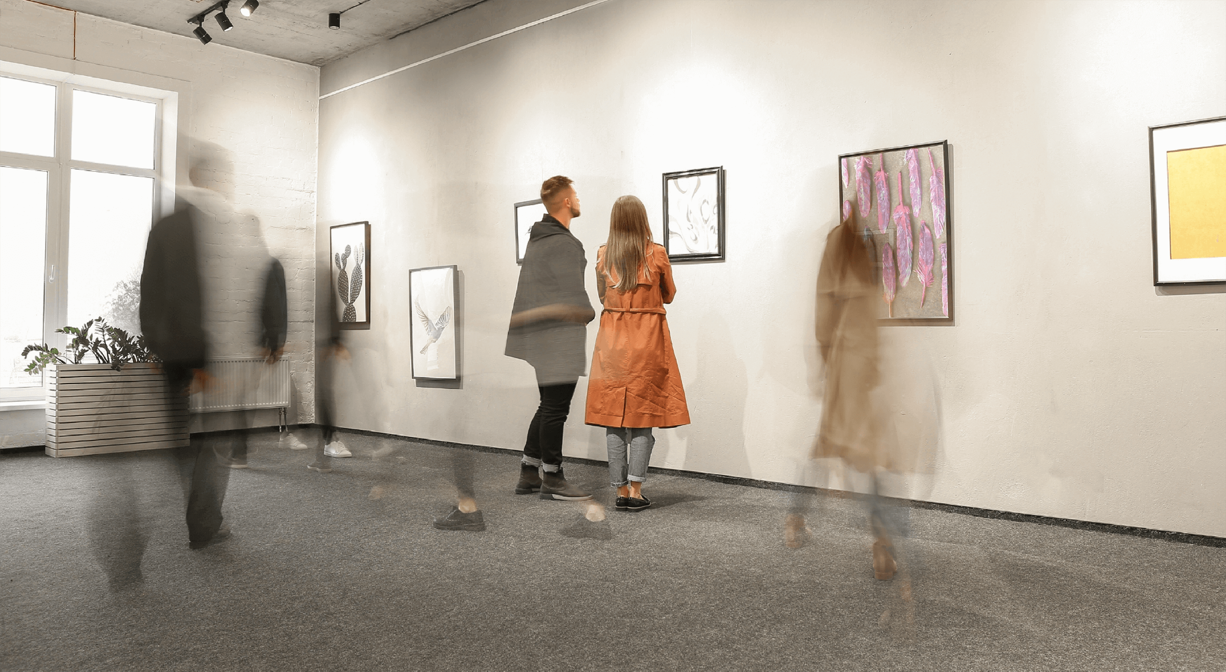 man with woman in orange coat viewing art at exhibition